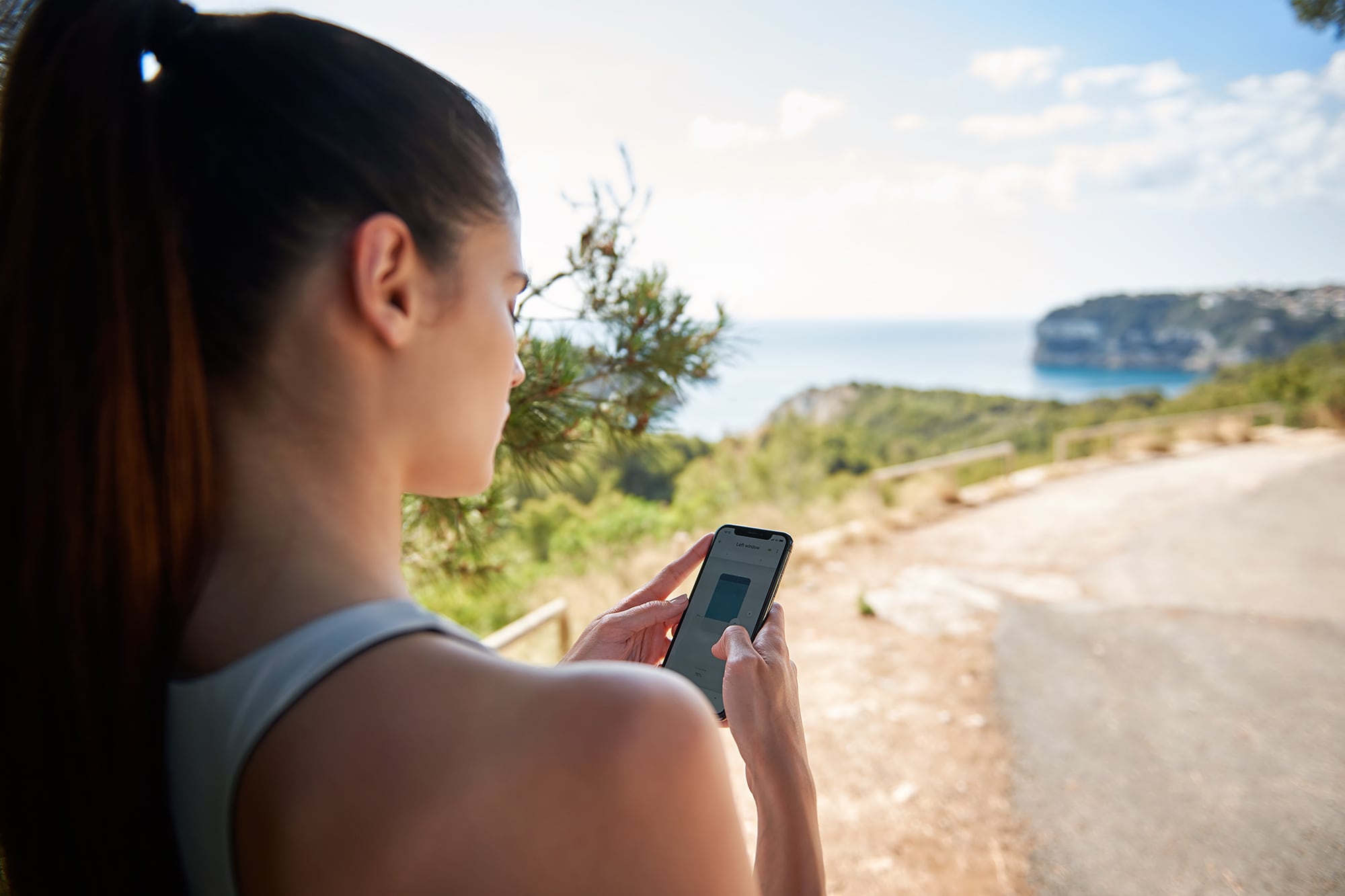 [Translate to Italienisch:] Frau steuert ihren Sicht-/Sonnenschutz von draußen über ihr Smartphone