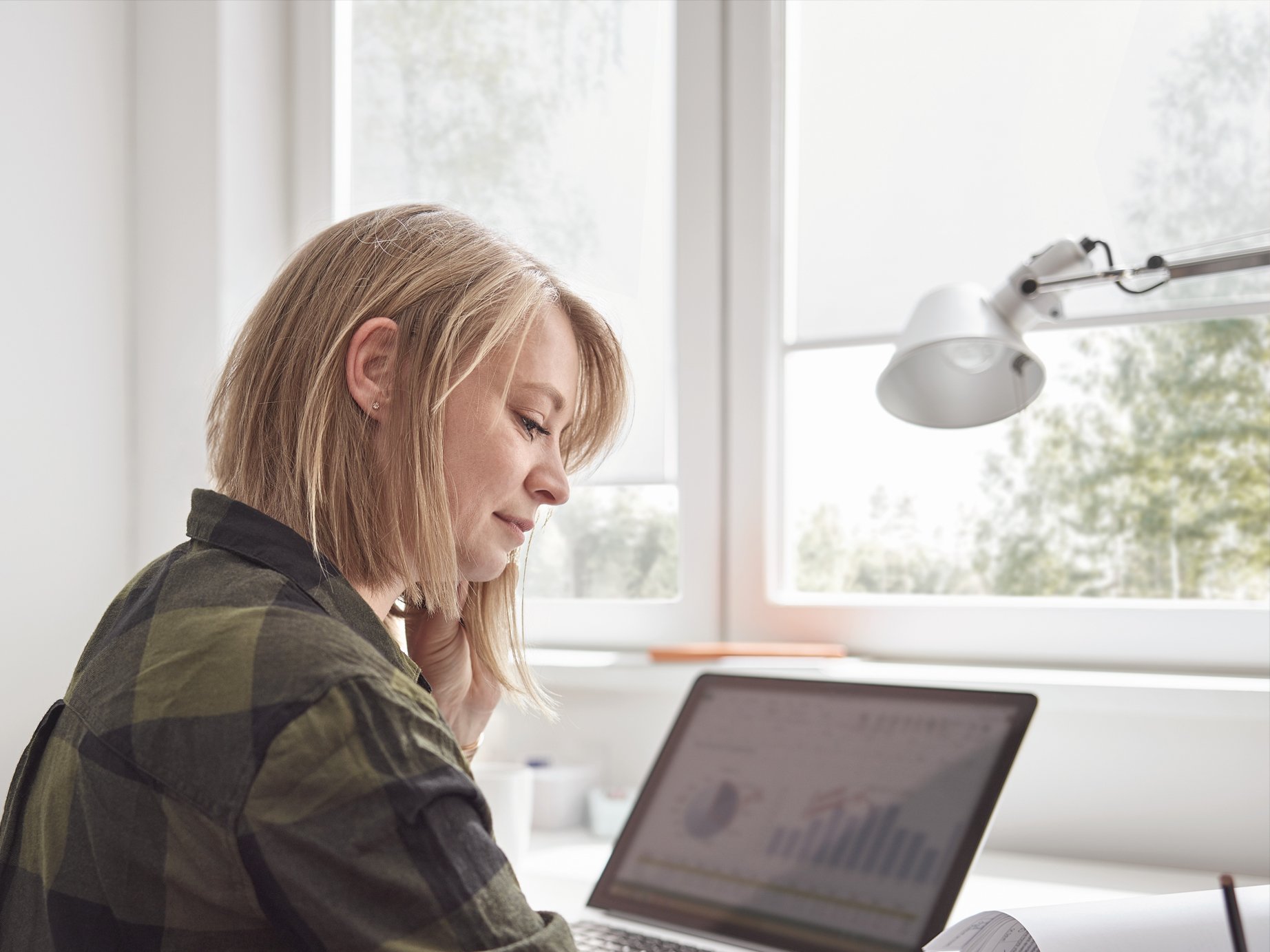 [Translate to Italienisch:] Frau arbeitet im Homeoffice mit microTex Rollos im Hintergrund