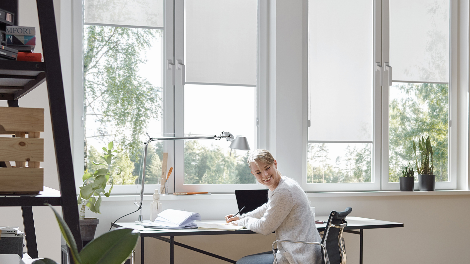 [Translate to English:] Frau sitzt im Homeoffice vor hellen KADECO-Rollos